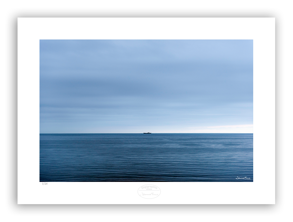 An image of a boat on the sea at the horizon line. Blue sea and blue clouds in a calm weather. 